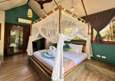 Standard cottage bedroom with bamboo framed king-size bed with draped mosquito netting and ceiling fan.