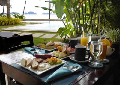 A table set for breakfast beside a pool with sea view.