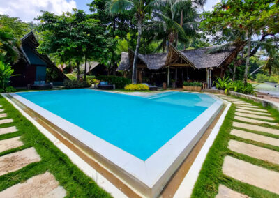 Swimming pool is surrounded by traditional cottages, beachfront restaurant and tropical trees.