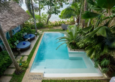 Beachfront swimming pool with sun loungers, surrounded by tropical vegetation